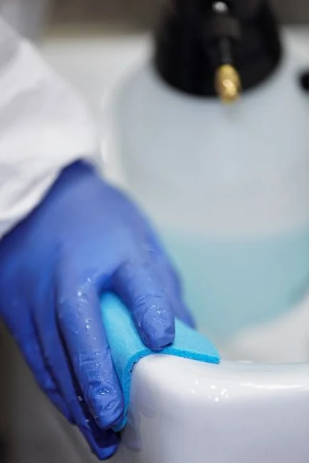 Anonymous person in yellow rubber gloves using simple sponge for cleaning mirror in bathroom